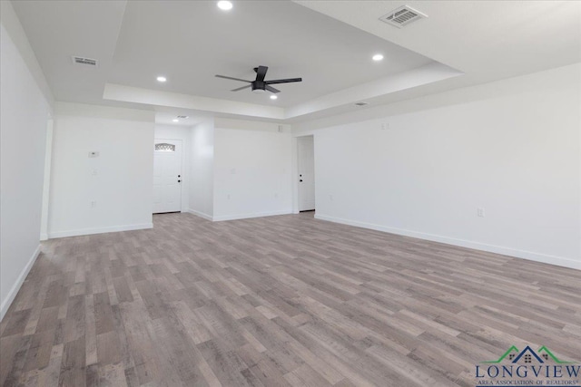 unfurnished living room featuring a tray ceiling, light hardwood / wood-style flooring, and ceiling fan