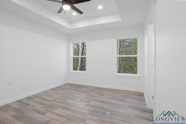 empty room with ceiling fan, light hardwood / wood-style floors, and a raised ceiling