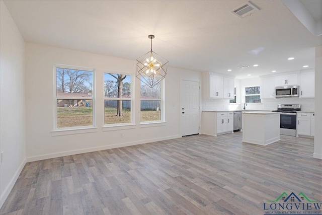 kitchen featuring stainless steel appliances, light hardwood / wood-style flooring, decorative light fixtures, tasteful backsplash, and white cabinets