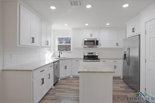 kitchen with white cabinetry, light stone countertops, stainless steel appliances, and a center island