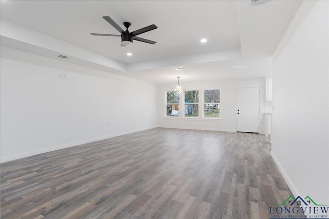 unfurnished living room featuring ceiling fan with notable chandelier, dark hardwood / wood-style floors, and a raised ceiling