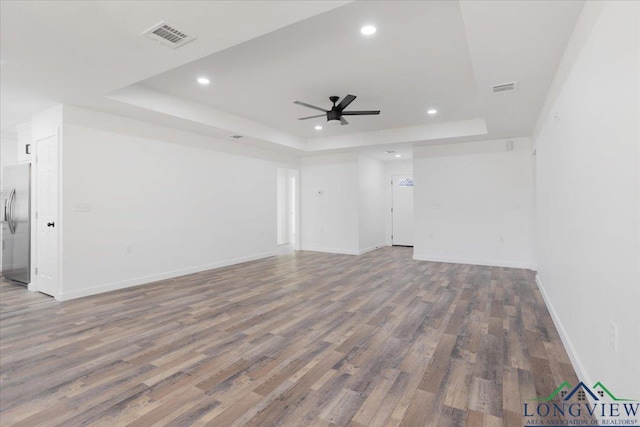 unfurnished living room with ceiling fan, a raised ceiling, and wood-type flooring