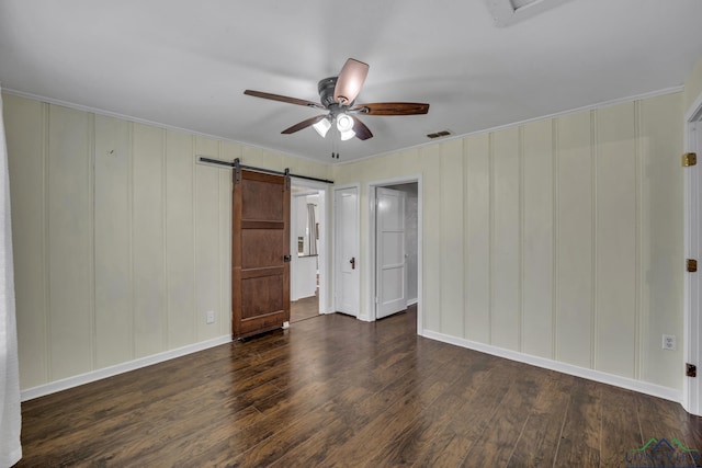 unfurnished bedroom with dark wood-type flooring, ceiling fan, and a barn door