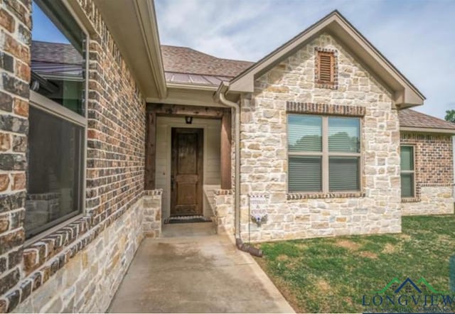 entrance to property with brick siding, stone siding, and a shingled roof