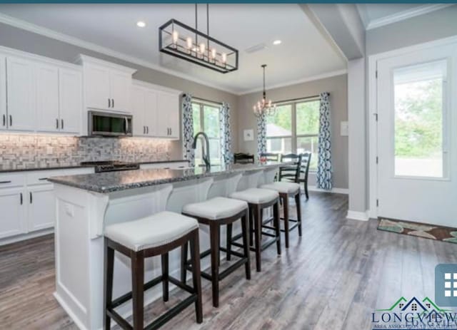 kitchen featuring hanging light fixtures, a kitchen breakfast bar, white cabinetry, and a kitchen island with sink