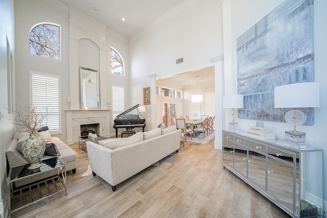 living area featuring crown molding, a towering ceiling, light wood-style floors, and a high end fireplace