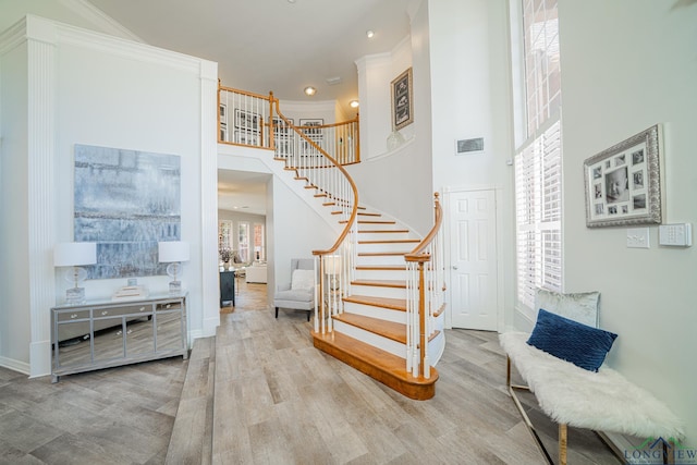 staircase with wood finished floors, baseboards, visible vents, ornamental molding, and a towering ceiling