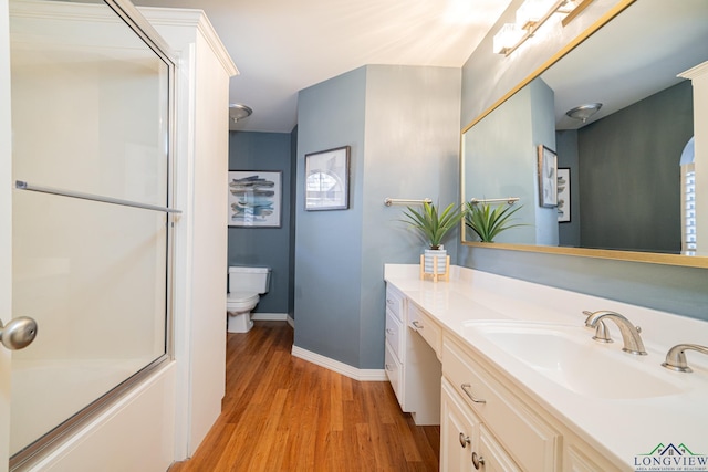 bathroom with a shower with shower door, vanity, toilet, and wood finished floors