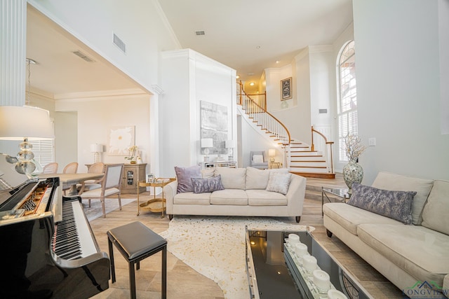 living room with stairway, wood finished floors, visible vents, a high ceiling, and crown molding