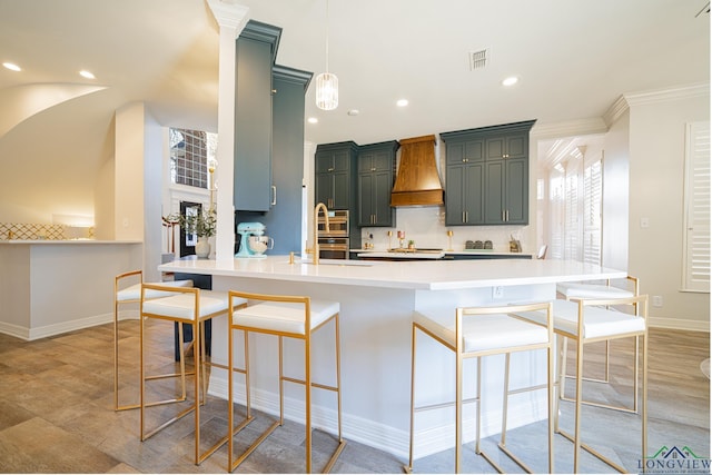 kitchen featuring visible vents, premium range hood, a breakfast bar, light countertops, and decorative backsplash