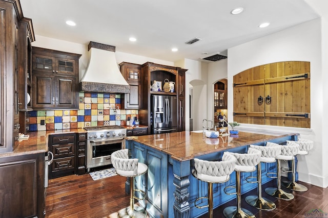 kitchen featuring appliances with stainless steel finishes, tasteful backsplash, a kitchen island, custom range hood, and a breakfast bar area