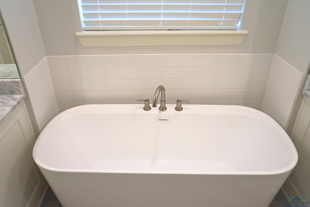 9173 Cave Branch Cv, Tyler, TX 75703 - bathroom with a soaking tub, vanity, tile walls, and wainscoting