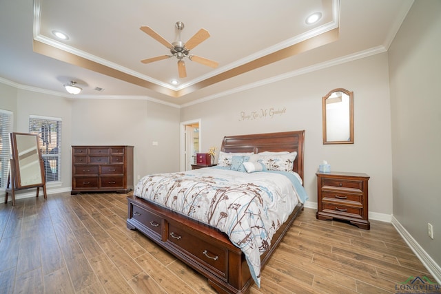 bedroom with light wood finished floors, a tray ceiling, and crown molding