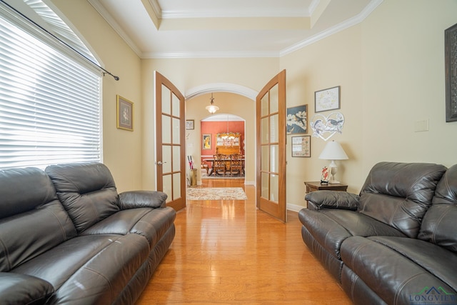 living room with arched walkways, a raised ceiling, crown molding, french doors, and light wood-type flooring