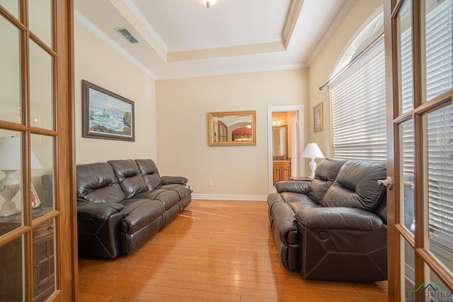 living area featuring light wood-type flooring, crown molding, visible vents, and a tray ceiling