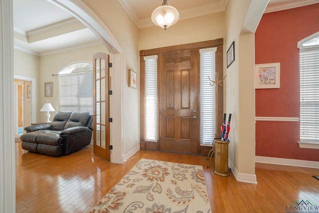 foyer entrance featuring light wood-type flooring, arched walkways, and crown molding