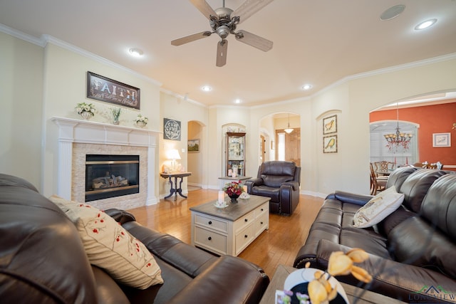 living area with arched walkways, crown molding, light wood-style flooring, and ceiling fan with notable chandelier