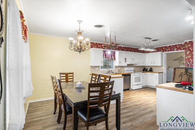 dining room with a chandelier, light wood finished floors, baseboards, ornamental molding, and stacked washer / drying machine