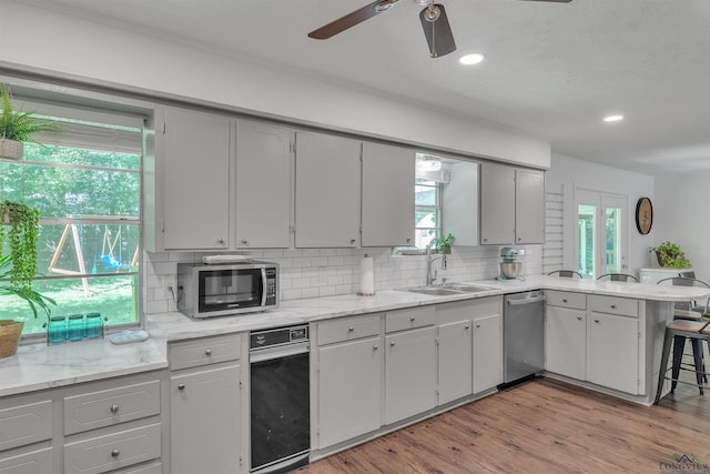 kitchen with stainless steel appliances, a peninsula, a sink, backsplash, and ceiling fan