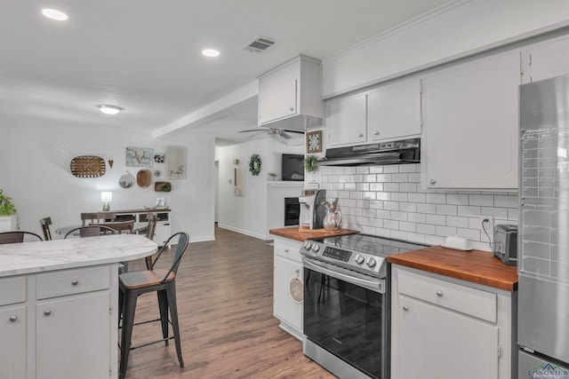 kitchen featuring butcher block countertops, decorative backsplash, appliances with stainless steel finishes, under cabinet range hood, and visible vents
