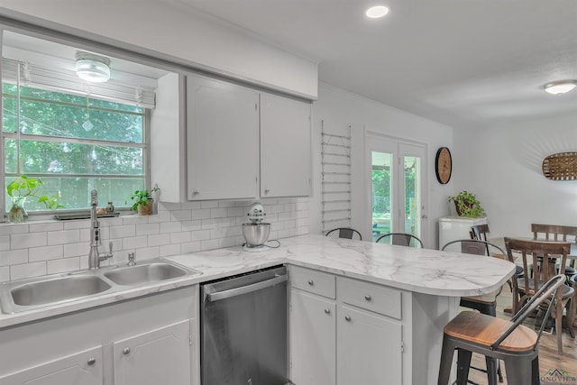 kitchen featuring a peninsula, a kitchen breakfast bar, a sink, backsplash, and dishwasher