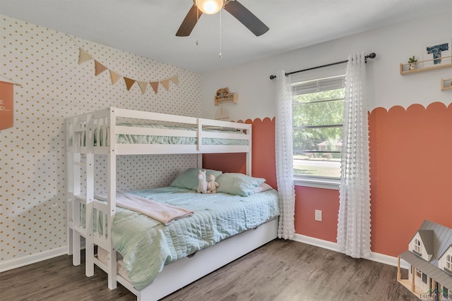 bedroom featuring baseboards, an accent wall, wood finished floors, and wallpapered walls