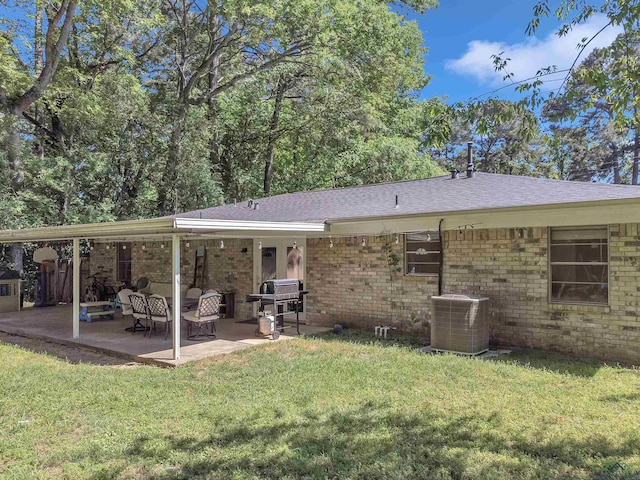 rear view of house featuring roof with shingles, central AC, brick siding, a yard, and a patio