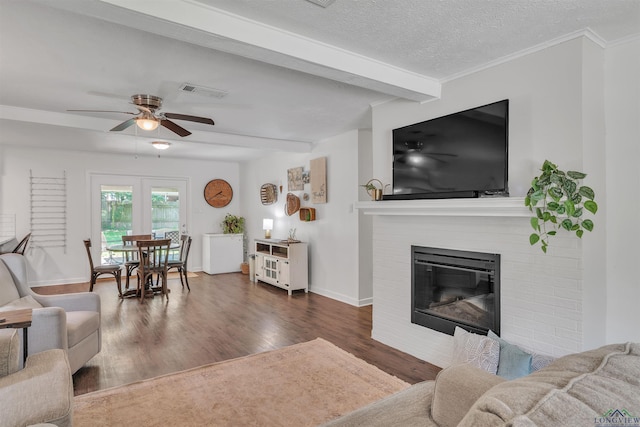 living room with wood finished floors, ceiling fan, a fireplace, beam ceiling, and visible vents