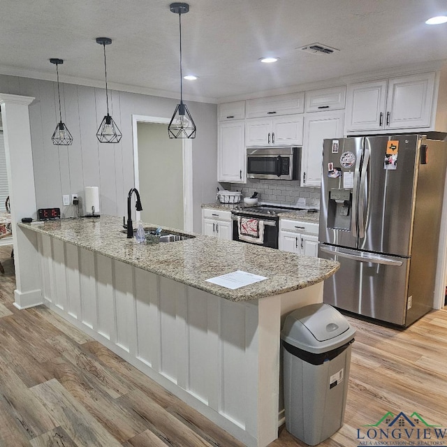 kitchen featuring appliances with stainless steel finishes, pendant lighting, white cabinetry, sink, and light stone countertops