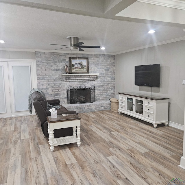 living room with ornamental molding, a brick fireplace, ceiling fan, and light hardwood / wood-style flooring