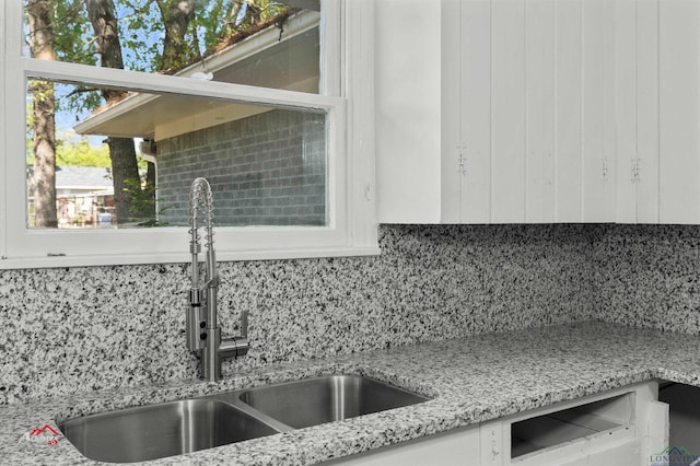 details featuring white cabinets, backsplash, light stone countertops, and sink