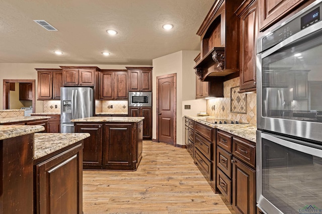 kitchen featuring dark brown cabinetry, stainless steel appliances, visible vents, a center island, and light wood finished floors