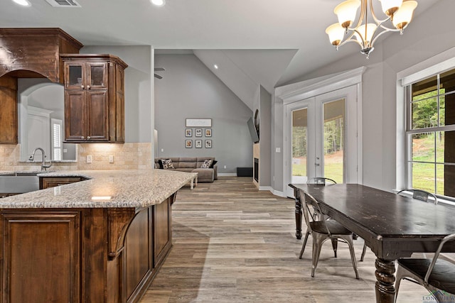 kitchen with decorative backsplash, french doors, vaulted ceiling, a chandelier, and hanging light fixtures