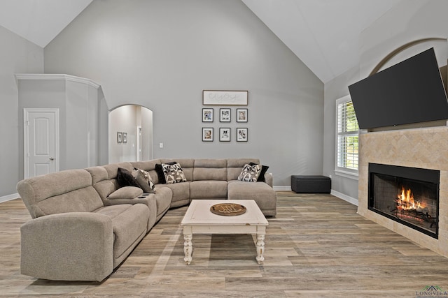 living room featuring light hardwood / wood-style floors, high vaulted ceiling, and a tiled fireplace