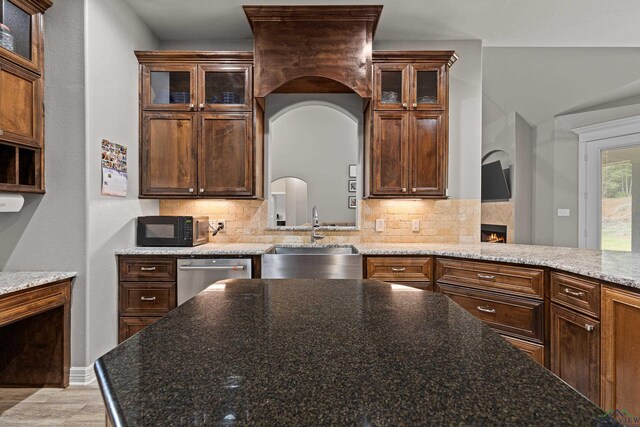 kitchen featuring stainless steel dishwasher, dark stone countertops, sink, and tasteful backsplash