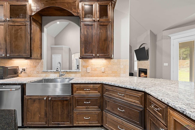 kitchen with decorative backsplash, light stone counters, vaulted ceiling, sink, and dishwasher