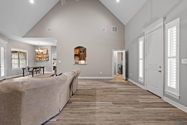 living room with light wood-type flooring, an inviting chandelier, high vaulted ceiling, and washer and clothes dryer