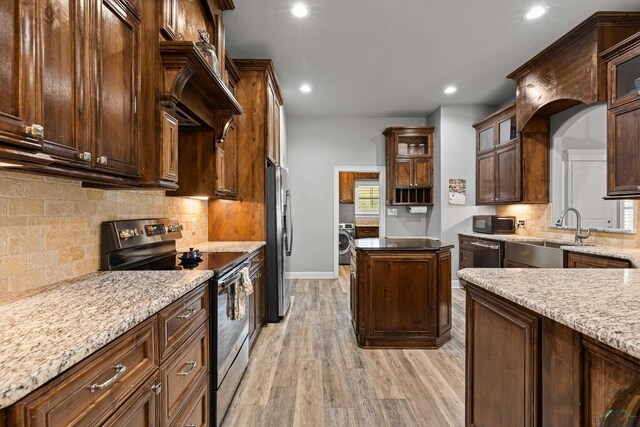 kitchen featuring sink, light stone countertops, light wood-type flooring, appliances with stainless steel finishes, and washer / clothes dryer