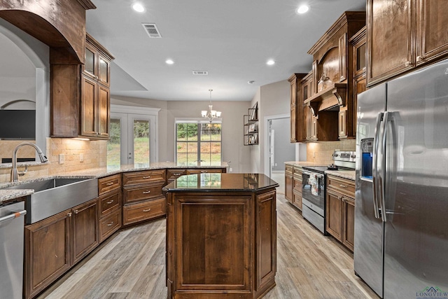 kitchen featuring light wood-type flooring, stainless steel appliances, sink, a kitchen island, and hanging light fixtures