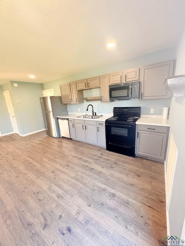 kitchen with black electric range, light countertops, light wood-style flooring, a sink, and dishwasher