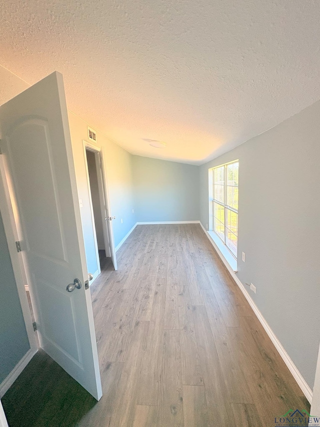 unfurnished room with a textured ceiling, baseboards, and wood finished floors