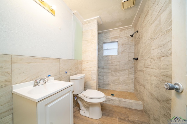 bathroom with vanity, a tile shower, tile walls, and toilet