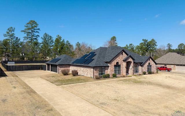 french country style house featuring a garage, solar panels, fence, driveway, and roof with shingles