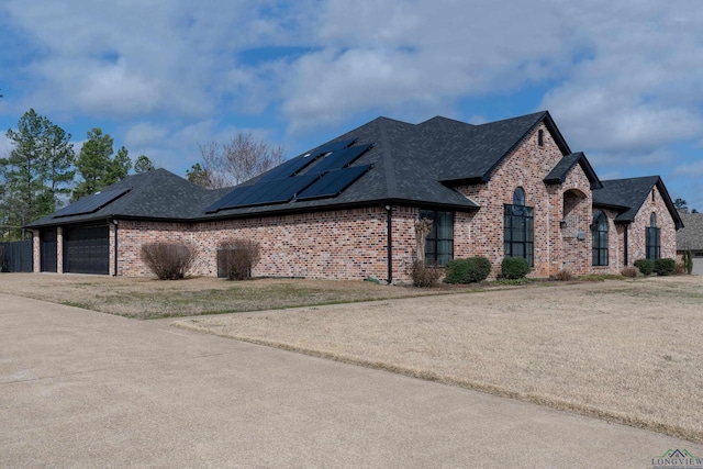 view of front of property featuring roof with shingles, a front lawn, solar panels, and brick siding