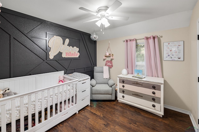 bedroom featuring a nursery area, dark wood-type flooring, and ceiling fan