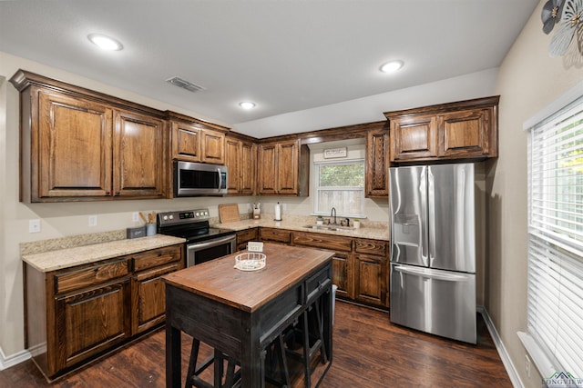 kitchen featuring dark wood-type flooring, sink, a kitchen island, light stone counters, and stainless steel appliances