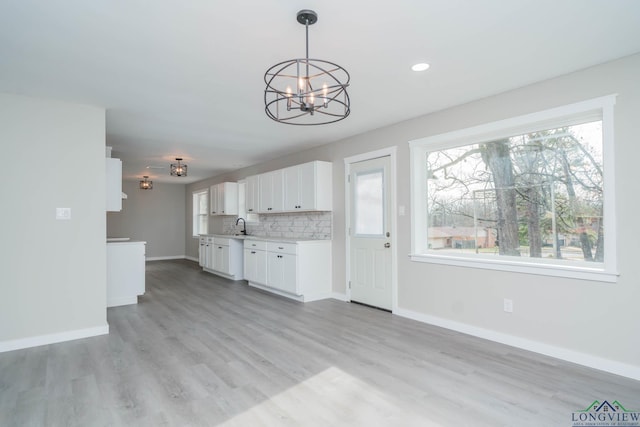 kitchen featuring light hardwood / wood-style flooring, decorative light fixtures, sink, backsplash, and white cabinets