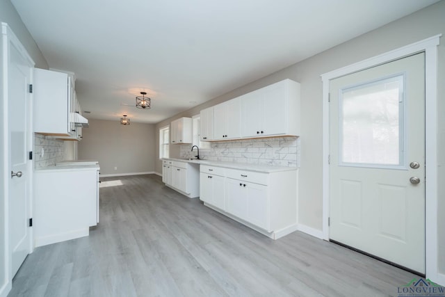 kitchen with white cabinets, backsplash, light wood-type flooring, and sink