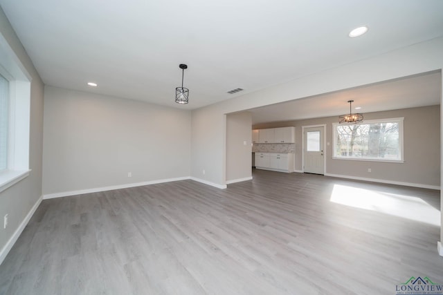 unfurnished living room featuring light wood-type flooring and an inviting chandelier