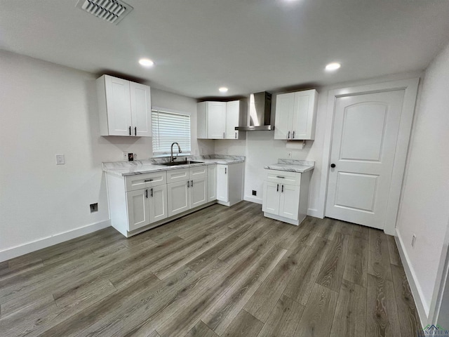 kitchen with white cabinets, wall chimney range hood, sink, dark hardwood / wood-style flooring, and light stone counters